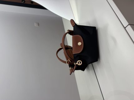 Black Longchamp Le Pliage Mini bag with brown accents on table.