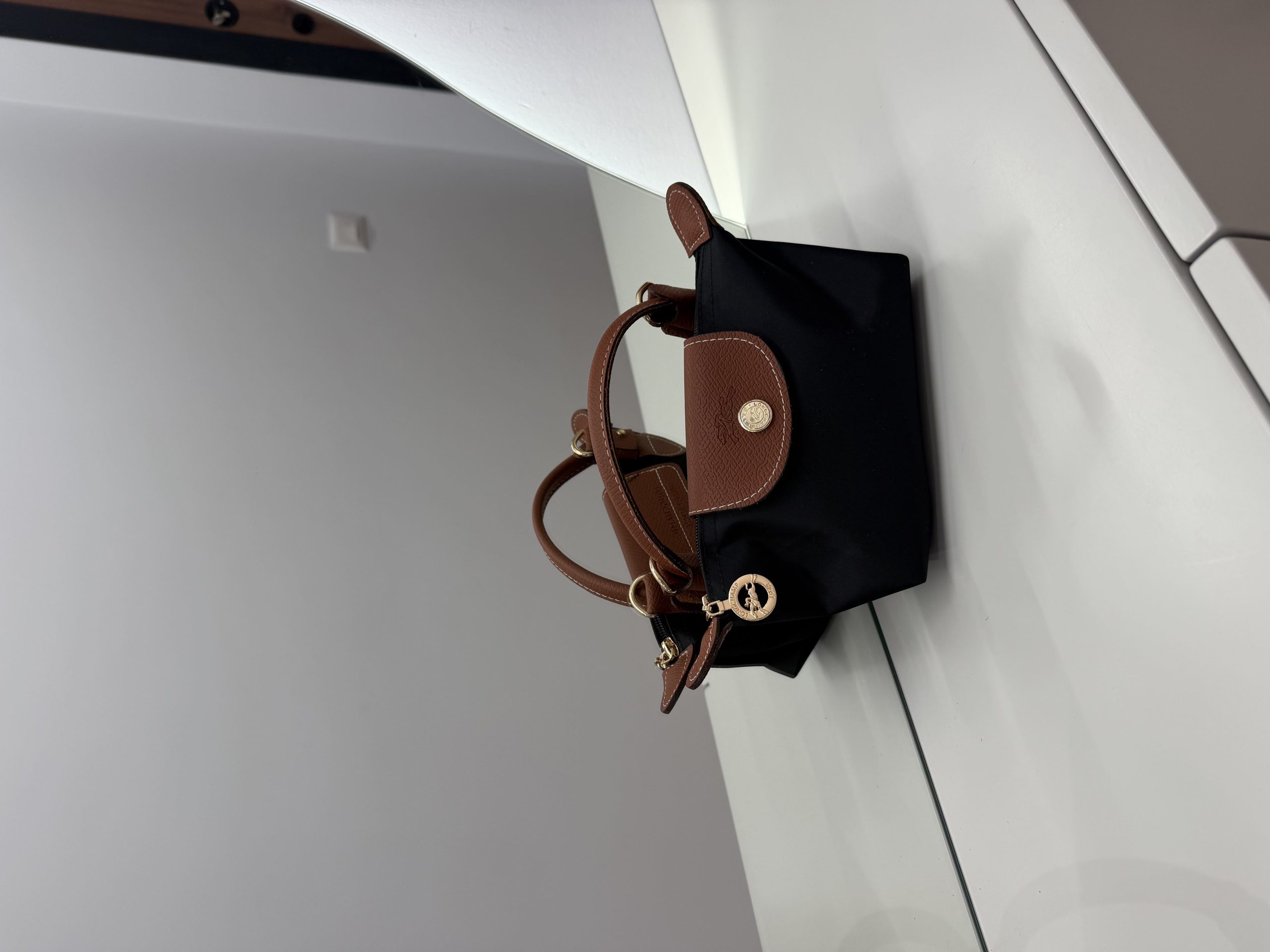 01_zezekafe Black Longchamp Le Pliage Mini bag with brown accents on table.