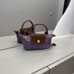 Çantë Longchamp Le Pliage Mini lila në një sipërfaqe të bardhë.