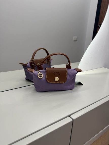Çantë Longchamp Le Pliage Mini lila në një sipërfaqe të bardhë.