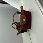 Bordo Longchamp Le Pliage Mini handbag on white surface.