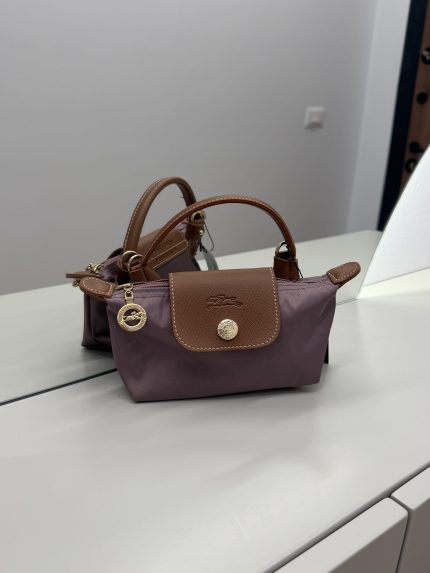 Çantë Longchamp Le Pliage Mini mauve në një sipërfaqe të bardhë.
