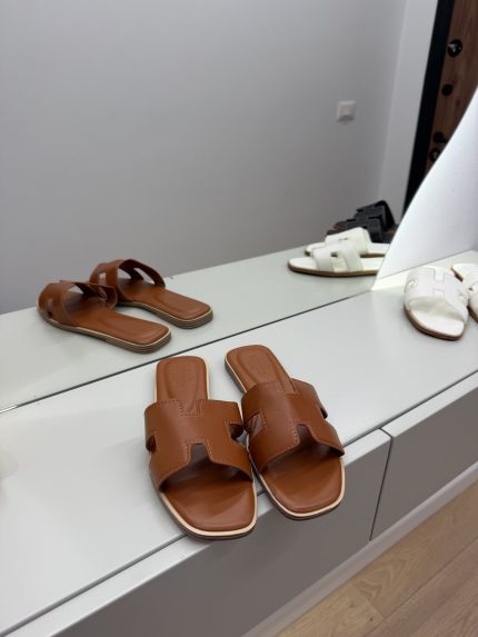 Hermes Oran Klasike brown sandals on display in a modern store.