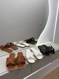 Hermes Oran Klasike sandals in brown, white, and black on display.