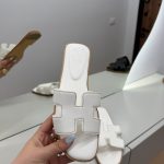 White Hermes Oran sandals displayed in a modern interior setting.
