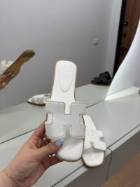 White Hermes Oran sandals displayed in a modern interior setting.