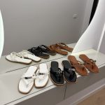 Hermes Kelly-Lock sandals in white, black, and brown on display.