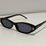 Chanel oval sunglasses, black frame, gold logo, stylish design.