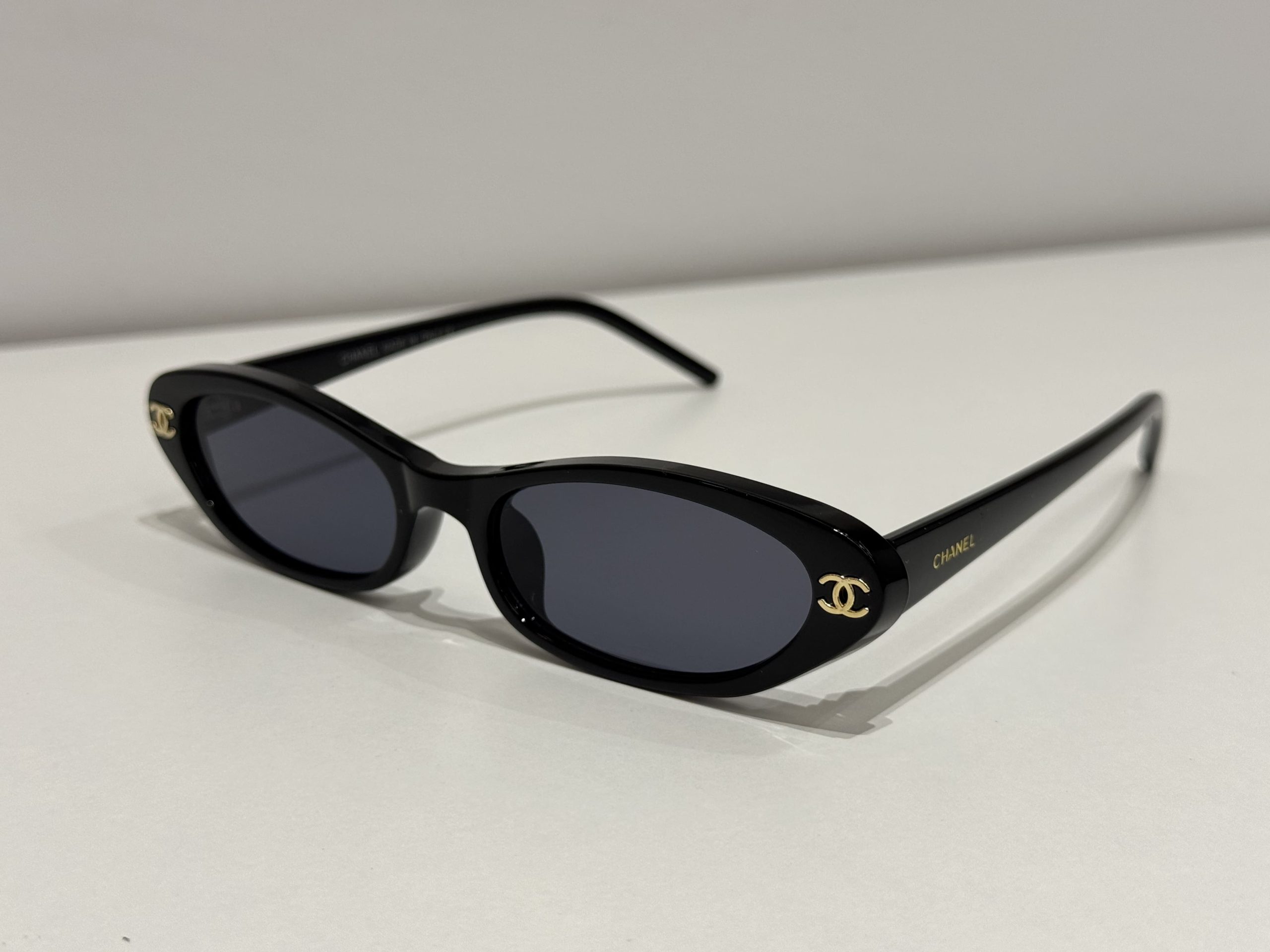 syze-chanel-oval-kryesore Chanel oval sunglasses, black frame, gold logo, stylish design.