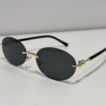 Rimless oval sunglasses with black lenses and gold accents.