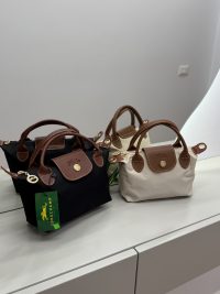 Çantë Femrash Longchamp handbags in black and beige on display.