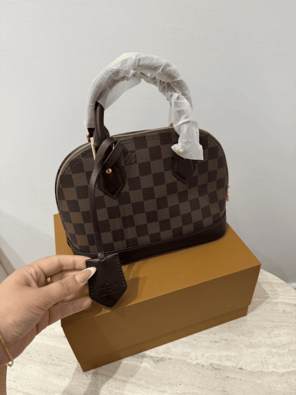 Louis Vuitton Alma Medium handbag on box, checkered pattern.