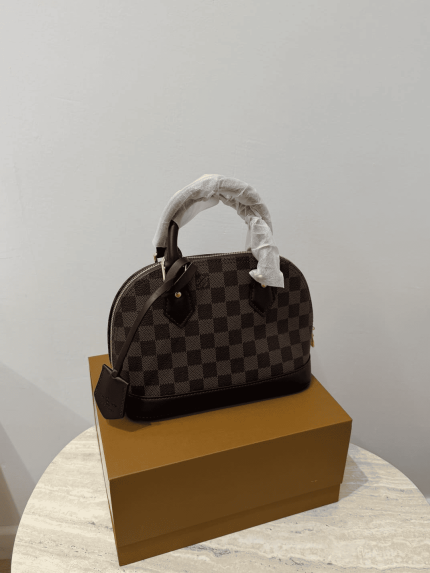 Louis Vuitton Alma Medium handbag on box, checkered pattern.