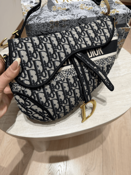 Canta Femrash Dior Saddle Oblique me dizajn elegant dhe akcenta ari.
