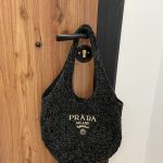 Prada Boucle beach bag hanging on wooden door handle.