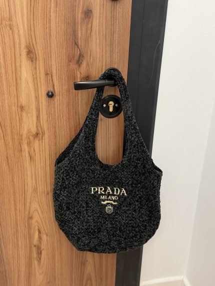 Prada Boucle beach bag hanging on wooden door handle.