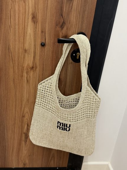 Miu Miu beach bag hanging on wooden door handle.