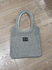 Elegant gray Miu Miu beach bag on wooden floor.