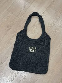 Black Miu Miu beach bag on wooden floor.