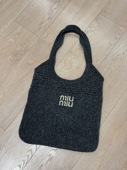 Black Miu Miu beach bag on wooden floor.