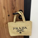Prada Mini beach bag hanging on wooden door handle.
