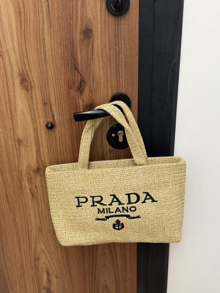 Prada Mini beach bag hanging on wooden door handle.