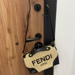 Fendi Roma beach bag with black accents hanging on wooden door.