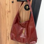 Çanta femrash YSL Hobo, elegancë dhe stil, ngjyrë e kuqe, në derë.
