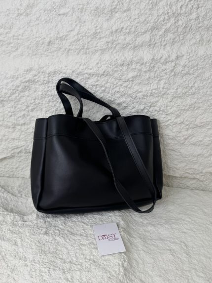 Elegant black tote bag on textured surface with tag.