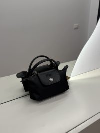 Black Longchamp Le Pliage XS handbag on mirrored surface.
