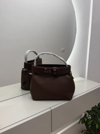 Brown bucket bag with studded strap on mirrored surface.