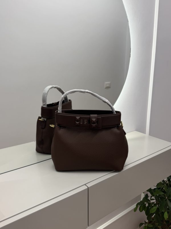 Brown bucket bag with studded strap on mirrored surface.