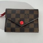 Checkered Goyard wallet with red button, elegant style.