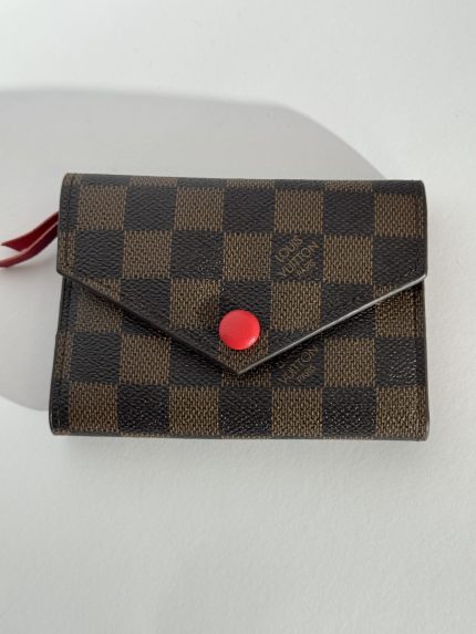 Checkered Goyard wallet with red button, elegant style.