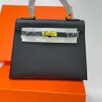 Çantë moderne HERMES KELLY 25 për femra, ngjyrë e zezë, mbi kuti portokalli.