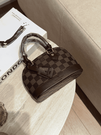 Çanta femrash Louis Vuitton Alma Mini e vendosur mbi një tavolinë mermeri.