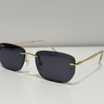 Syze dielli Ray-Ban me kuadrin e artë dhe lentet e errëta.
