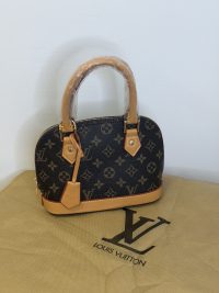 Louis Vuitton Alma BB handbag with shoulder strap on display.