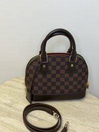 Louis Vuitton Alma BB handbag with shoulder strap on table.