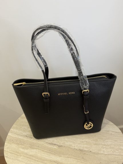 Black Michael Kors Jet Set tote bag on table.