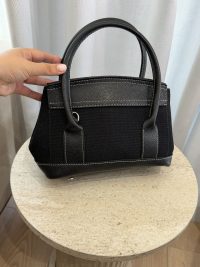 Elegant black canvas handbag with leather accents on table.