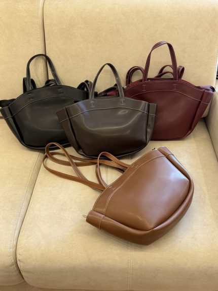Leather university bags in black, brown, burgundy, and tan on beige sofa.