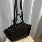 Black leather university bag with long handles on table.