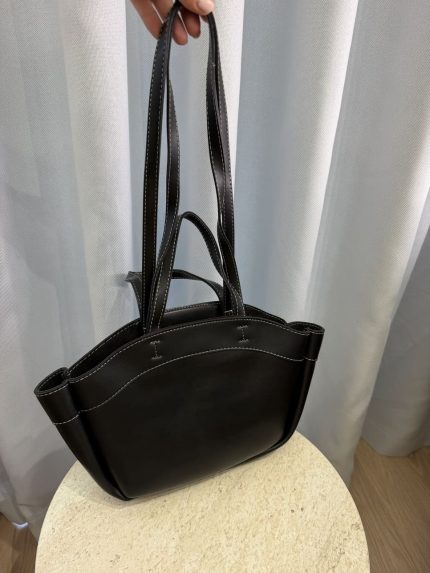 Black leather university bag with long handles on table.