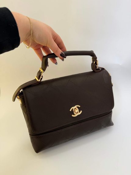 Chanel dark brown flap bag with handle and gold logo.