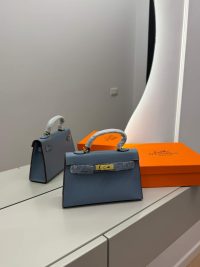Hermès Mini Kelly blue handbag with orange box on mirrored surface.