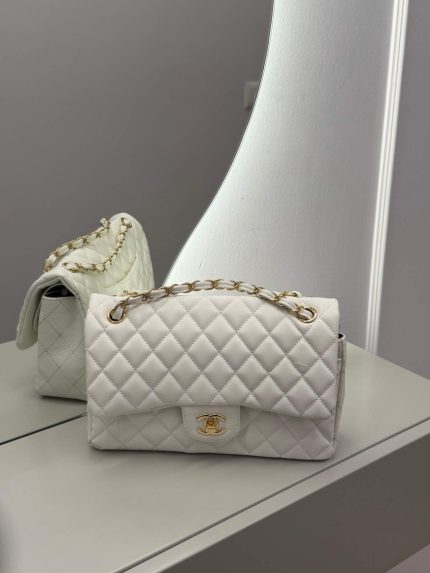 Chanel Classic Flap white bag with gold chain on mirror surface.