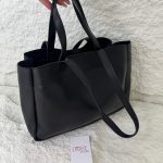 Black tote bag with double straps on textured background.