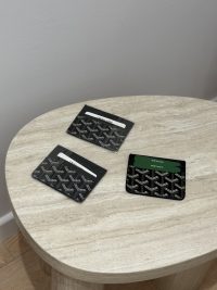 Goyard unisex cardholders on round wooden table, elegant and functional design.