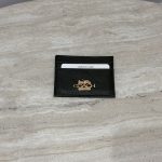 Black Coach cardholder with gold logo on marble surface.